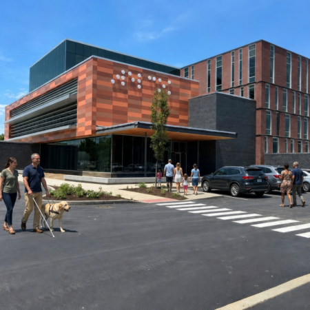 Photo of the front of the Dot Experience building with people walking in — some with canes or guide dogs, some families, and some individuals.
