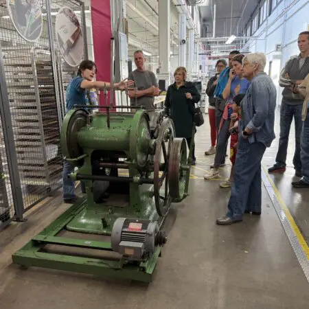 A group of people are standing and looking at an old braille embossing machine on a factory tour at American Printing House for the Blind